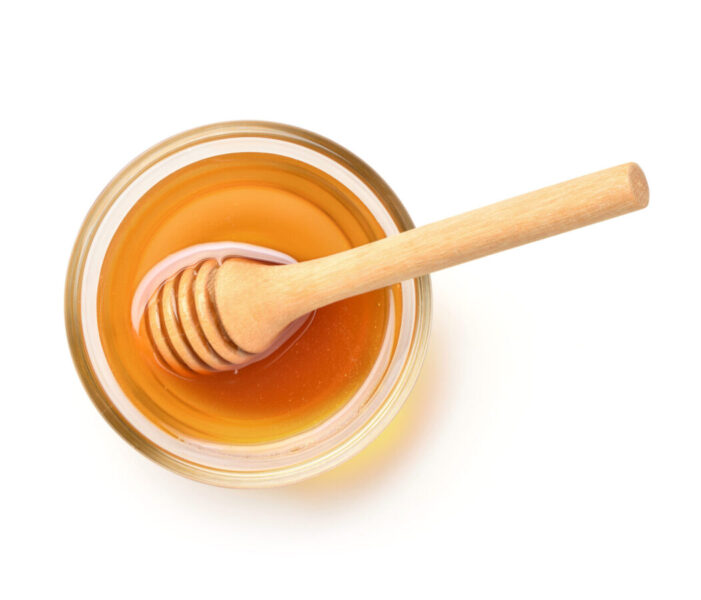 Glass bowl of pure honey with honey dipper isolated on white background. Clipping path.
